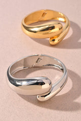 Polished gold metal bangle featuring a modern twist design

