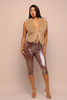 Woman wearing a beige fur vest and shiny brown leggings against a beige background