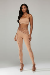 Woman wearing a beige outfit with ruffled pants on a plain background