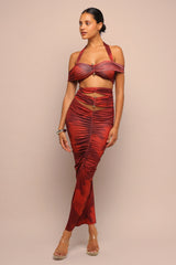 Woman wearing a red dress with a halter top and ruched skirt on a beige background