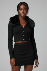 Woman wearing a black outfit with a fur collar against a gray background