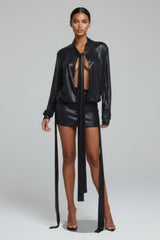 Model wearing a black leather outfit with a long coat and shorts on a white background