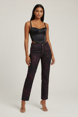 Woman wearing a black satin top and patterned pants on a light gray background