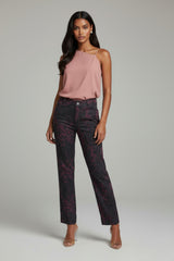 Woman wearing a pink top and dark patterned pants on a gray background