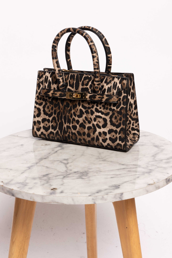 eopard print handbag placed on a marble table, featuring a structured design and gold hardware.