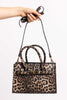 Leopard print handbag with a detachable shoulder strap and gold accents, held by hand.