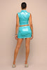 Person wearing a turquoise outfit with a matching top and skirt on a beige background