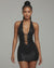 Model walking in black halter mini dress with deep plunge neckline and ladder strap cutouts, highlighting bodycon fit and glossy lace texture