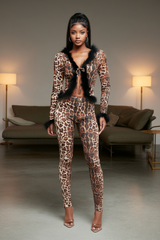Woman wearing a leopard print outfit with fur trim in a modern living room setting.