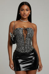 Woman wearing a strapless black and silver patterned top with a black skirt on a gray background